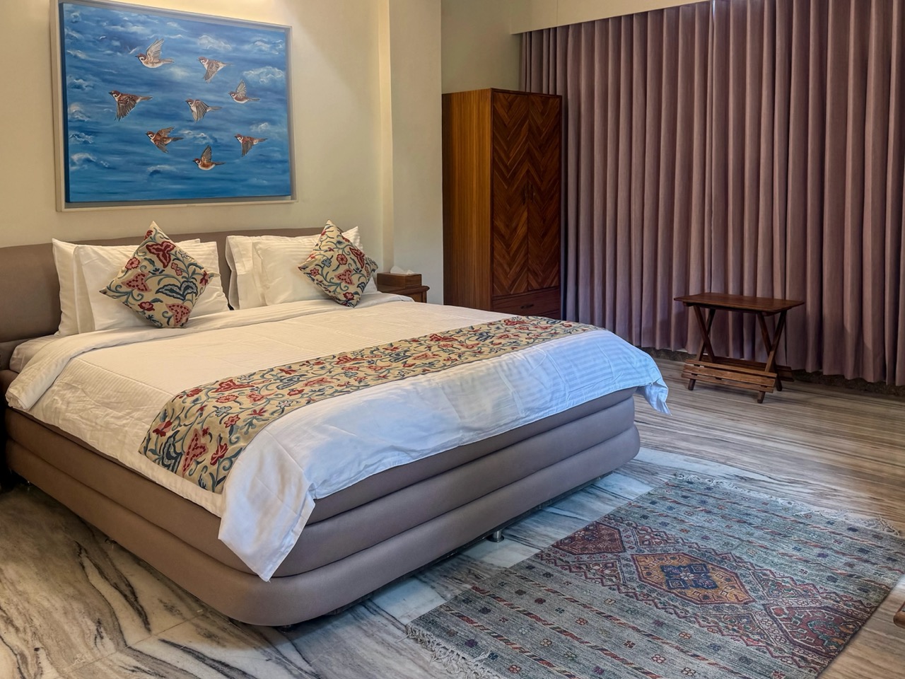 Rajnigandha suite at ArtRest Ahmedabad with a warm upholstered bed and original artwork.